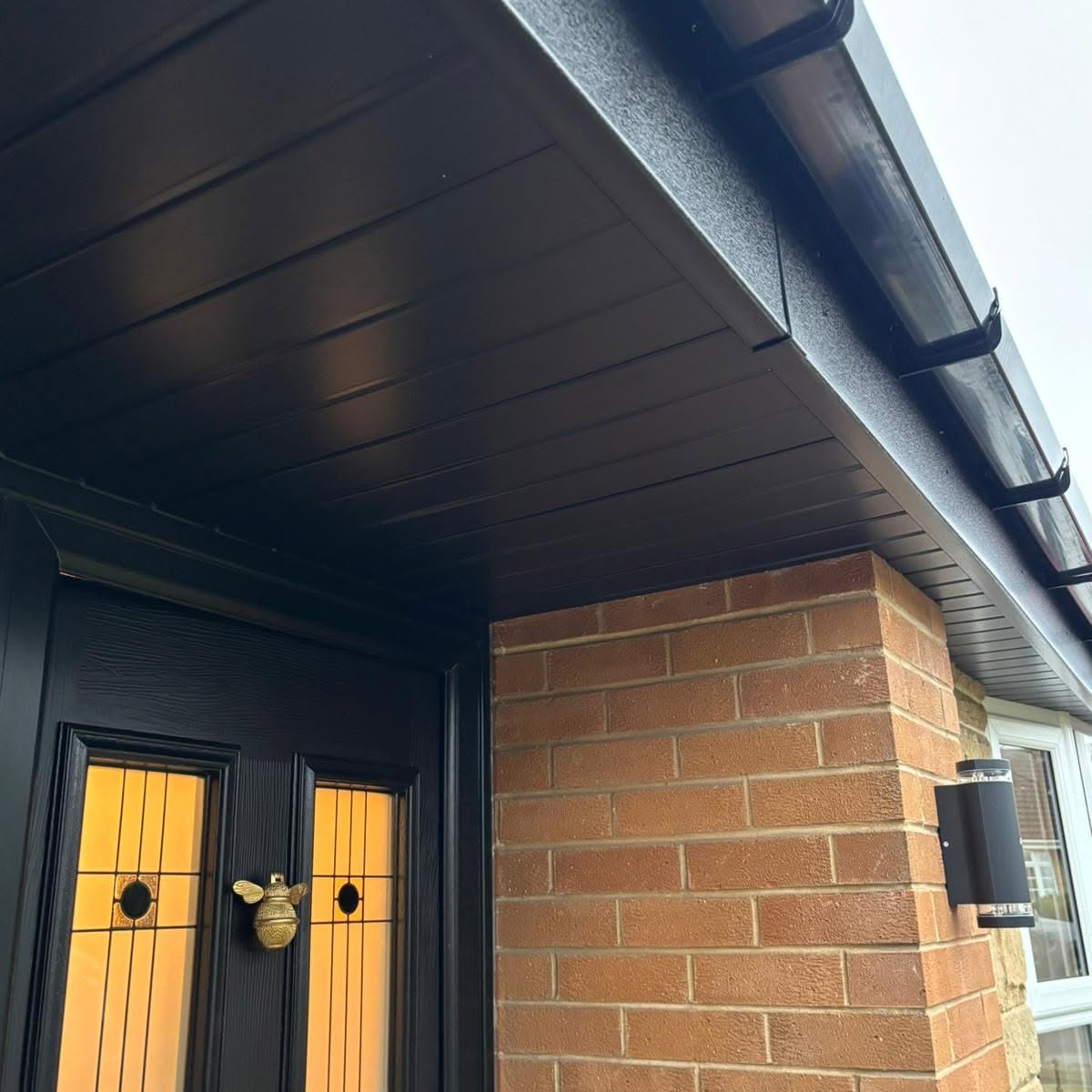 Black soffit porch ceiling and guttering above a composite front door